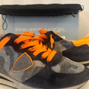 Unika Philippe Model  - Philippe Model sneakers i camouflage och orange detaljer (Går att byta skosnören om du ej gillar dessa) väldigt unika och snygga, Säljer i befintligt skick, vid frågor och funderingar tveka ej, dustbag och box medföljer!