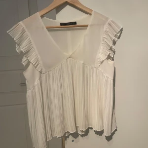 Vit blus med volangdetaljer - Säljer en superfin vit blus med volangdetaljer på ärmarna. Den har en v-ringad design och är perfekt för både vardag och fest.❤️‍🔥