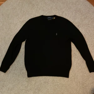 Svart tröja från Ralph Lauren - Säljer en stilren svart tröja från Ralph Lauren i merinoull. Perfekt för både vardag och festliga tillfällen. Tröjan har en klassisk design med långa ärmar och en liten broderad logga på bröstet. Supermjuk och bekväm att bära!