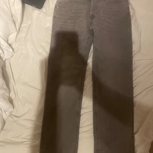 Grå jeans från Jack & Jones - Säljer ett par snygga grå jeans från Jack & Jones i nytt skick. De har en tapered passform och är midwaist. Byxorna har knappar istället för dragkedja och är perfekta för både vardag och fest. De är gjorda i ett bekvämt denim-material.