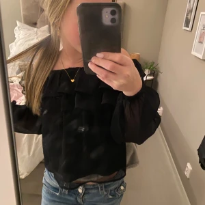 Svart offshoulder blus  - Säljer en snygg svart offshoulder topp från Gina Tricot i storlek 134/140. Toppen har volangdetaljer och är perfekt för både vardag och fest. Materialet är lätt och luftigt, vilket gör den bekväm att bära. Passar perfekt till jeans eller kjol för en stilren look. Jag är 151 och tycker den är lite liten men annars perfekt!