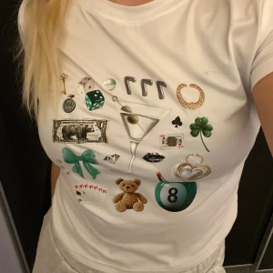 Vit t-shirt med tryck - Säljer en cool vit t-shirt med massor av detaljerade tryck som en martiniglas, nallebjörn, fyrklöver och spelkort. Perfekt för en avslappnad dag eller en rolig festkväll. Superbekväm och lätt att matcha med jeans eller shorts!