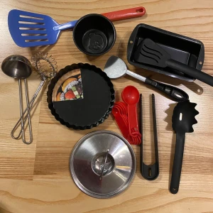 Köksredskap lek, barn  - En samling köksredskap i olika färger och material. Inkluderar en blå stekspade, en röd handvisp, en svart brödform, och flera måttskedar. Perfekt för den som älskar att laga mat och baka! Tyvärr fattas kastrullen, ingen aning om vart den tagit vägen! 