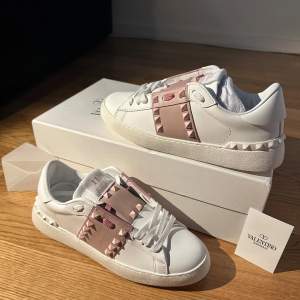 Säljer ett par snygga Valentino Rockstud sneakers i vitt läder med rosa detaljer. Skorna har de ikoniska nitarna och en stilren design. Perfekta för att ge din outfit en lyxig touch. De är i nytt skick och kommer med originalförpackning. Priset går att förändras