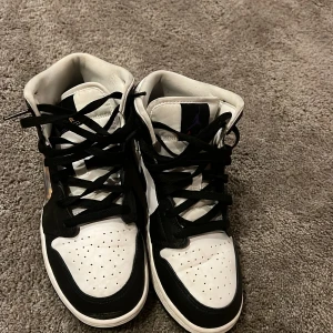 Nike Air Jordans i svart och vitt - Säljer ett par coola Nike Air Jordans i svart och vitt. Skorna har en unik design med ett färgglatt mönster på sidan och klassisk snörning. Perfekta för både vardag och fest! De är i mycket bra skick och redo för nya äventyr. det är en junior sko som har storlek 40.