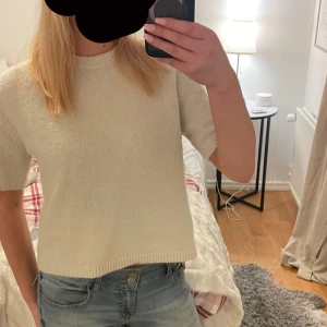 Vit stickad tröja - Säljer en superfin vit stickad tröja i bra skick. Den har korta ärmar och en normal passform, perfekt för vår och sommar. Tröjan är enkel och stilren, vilket gör den lätt att matcha med olika outfits. Lite åt krämvit/beige hållet