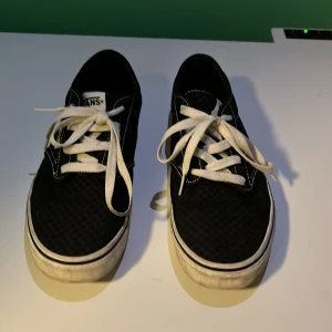 Svarta Vans sneakers med rutigt mönster storlek 38,5 - Säljer ett par klassiska svarta Vans sneakers i bra skick. De har ett coolt rutigt mönster och vita snören. Perfekta för vardagsbruk och ger en skön streetstyle-look. Sulan är lite smutsig men annars är de i fint skick. Passar perfekt för både vår och höst!