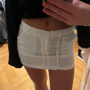 Vit kortkjol med snörning - Säljer en superfin vit kortkjol med snörning framtill. Perfekt för sommaren eller en utekväll! Kjolen har en tight passform och är i mycket bra skick. Den är gjord av ett bekvämt material som sitter snyggt på kroppen.