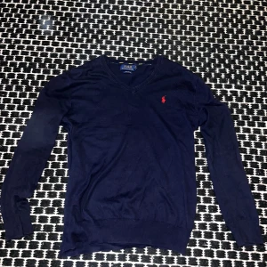 Mörkblå tröja från Ralph Lauren - Säljer en snygg mörkblå tröja från Ralph Lauren i storlek s men passar m med klassisk v-ringning. Den har en liten röd logga på bröstet och är gjord i mjuk bomull. Perfekt för både vardag och lite finare tillfällen. Passar bra till jeans eller chinos! 