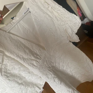 Vit klänning från Showpo - Säljer en superfin vit klänning från Showpo i storlek M. Den har en v-ringad design med puffiga kortärmar och en dragkedja i ryggen. Perfekt för sommarens fester eller studentfiranden! Materialet är strukturerat och ger en lyxig känsla. Helt ny med tag kvar!