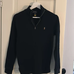 Svart tröja från Polo Ralph Lauren - Säljer en stilren svart tröja från Polo Ralph Lauren i storlek L i junior storlek. Tröjan har en dragkedja vid halsen och det klassiska Polo-logotypen broderad på bröstet. Perfekt för både vardag och lite finare tillfällen. Passar bra till höst och vinter. Nypris ligger på ungefär 2000kr.🙌