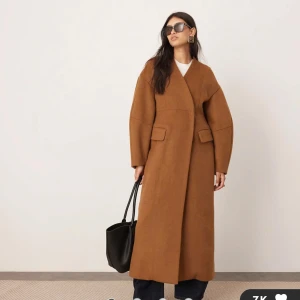 Brun kappa - Säljer en snygg brun och lång kappa som är helt ny. Perfekt för höst och vintern, och ger en stilren look. Passar både till vardags och festliga tillfällen. 52% ull, lite stor i storleken.