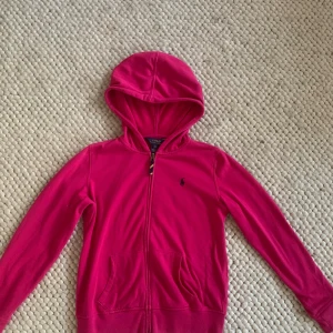 Rosa hoodie från Polo Ralph Lauren - Säljer en snygg rosa hoodie från Polo Ralph Lauren i storlek XL barnstorlek(16år) passar xs. Den har en dragkedja framtill och en klassisk huva. Perfekt för en avslappnad stil och passar bra till både höst och vår. Hoodien är i mycket bra skick och redo för nya äventyr!