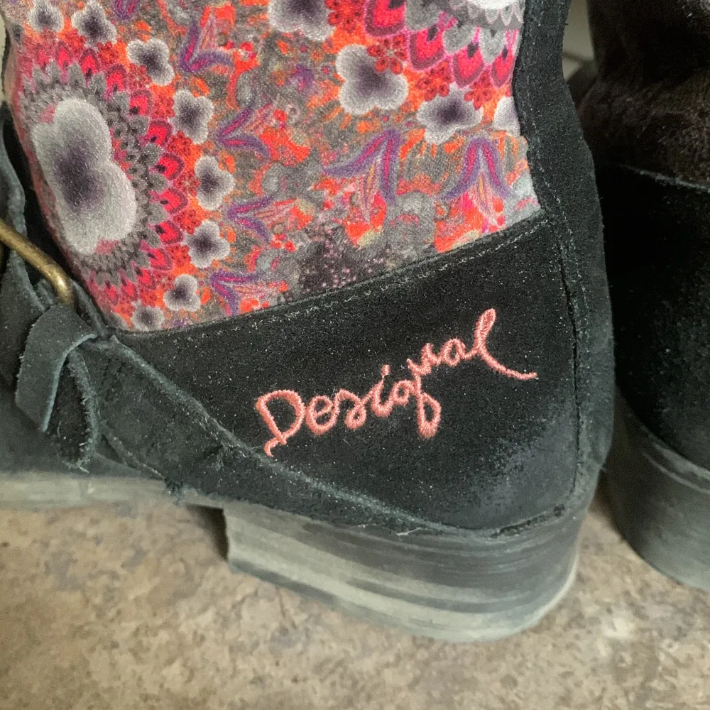 Snygga boots från Desigual i svart mocka med färgglatt mönster på skaftet. De har spännen i bronsfärg och en unik design med broderade detaljer. Perfekta för att liva upp höst- och vinteroutfits! Pris kan diskuteras.. Skor.