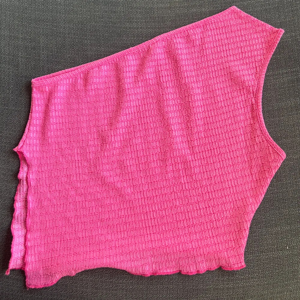 Säljer en superfin rosa oneshoulder topp med slits på ena sidan material. Perfekt för sommaren eller en festkväll! Toppen har en asymmetrisk design som ger en unik look.. Toppar.