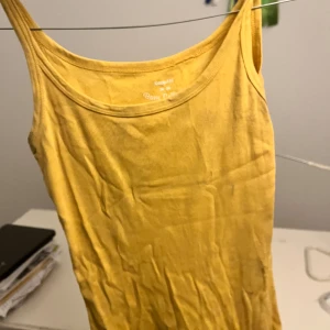 Gul ribbad linnetopp - Säljer en solgul ribbad linnetopp i bomull. Perfekt för sommardagar eller som ett lager under en tröja. Toppen har en enkel och stilren design med smala axelband. Den är i bra skick och passar till både jeans och kjol. Perfekt för en avslappnad look!