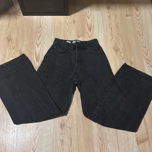 Svarta jeans från Bershka - Säljer ett par svarta jeans från Bershka i storlek EUR 36. De har en cool, sliten look med revor på benen och en hög midja. Perfekta för en avslappnad stil med en vintagekänsla. Passar bra till både vardag och fest! (Köpare står för frakt)