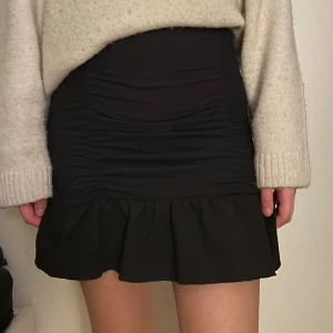 Svart tajt kjol - Svart tajt kjol med struktur fram och bak, går ut längs ner som en stor volang. Använd fåtal gånger.