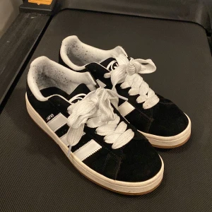 Svarta Adidas Campus sneakers - Säljer ett par svarta Adidas Campus sneakers i bra skick. Enbart använda fåtal gånger men lite steumpludd som fastnat i hälen(se bild) både svarta och vita skosnören följer med🥰🥰