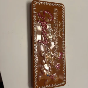 Gingerbread Extra Spicy ögonskuggspalett - Superfin ögonskuggspalett från Too Faced med 18 olika nyanser. Perfekt för höst och vinter med sina varma, kryddiga toner. Paletten har en söt design med pepparkaksgubbar och en inbyggd spegel. Färgerna är både matta och skimrande, vilket gör den idealisk för både vardag och fest.