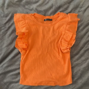 Orange ribbad topp från Zara - Säljer en superfin orange ribbad topp från Zara i storlek S. Den har volangdetaljer vid ärmarna som ger en söt touch. Toppen är i mycket bra skick!