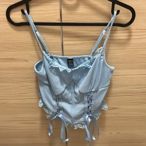 Ljusblå linne från Shein - Säljer en superfin linne från Shein i storlek M. Toppen har smala axelband som går att justera och är dekorerad med spetsdetaljer och snörning framtill. Den är ribbad och har en söt volangkant längst ner. Använd en gång