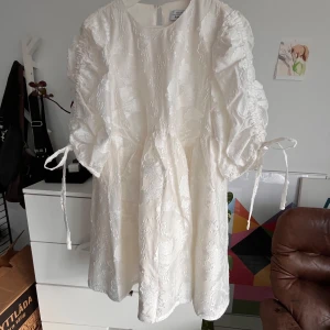 Vit klänning med broderade detaljer - Superfin vit klänning med broderade blommor och puffiga trekvartsärmar. Den har knytband vid ärmarna för en söt touch. Perfekt för sommarens fester eller studentfirande! 💐Endast använd en gång, nypris 1390kr