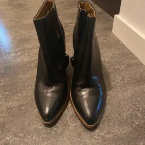 Snygga svarta boots i skinn från Mango med dragkedja på sidan. De har en träfärgad klack och spetsig tå, vilket ger en elegant look. Perfekta för höst och vinter, både till vardags och fest. Skorna är i mycket bra skick och redo för nya äventyr!