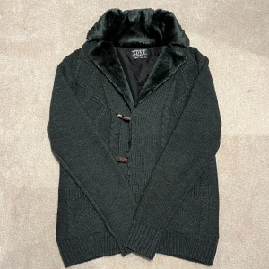 Fodrad Cardigan med Päls - Säljer en snygg grå fodrad cardigan med pälsfoder och träknappar. Koftan har ett flätmönster på framsidan och ribbade muddar. Perfekt för kyliga dagar! Väldigt sällsynt!!! Vid minsta fråga eller fundering hör av er🤝