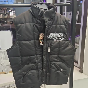 Svart quiltad väst från Yakuza - Säljer en svart quiltad väst från Yakuza med broderad text på både fram- och baksidan. Västen har dragkedja och knappar framtill samt två fickor. Perfekt för en cool och avslappnad stil. Material m: 100% Polyester. Kanske lite mindre I storleken.