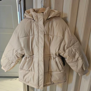 HELT NY Beige pufferjacka från NA-KD - HELT NY! Säljer en snygg beige pufferjacka från NA-KD. Jackan är i en oversized modell samt har en justerbar dragsko i midjan för perfekt passform. Passar även M/38 skulle jag säga.
