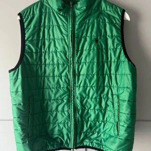 Grön quiltad väst från Conte of Florence - Snygg grön quiltad väst från Conte of Florence. Västen har en dragkedja framtill och är perfekt för en sportig look. Den är lätt och bekväm, idealisk för lager-på-lager under kyligare dagar.