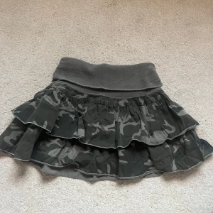 Camouflage kjol med volanger från Bershka - Snygg kortkjol i camouflage från bershka med volanger och bred ribbad midja. Ett litet hål i resåren, syns på sista bilden. Midjemått: stretchigt ogra resår därav från 32-40 cm rakt över. Längd: 32cm.