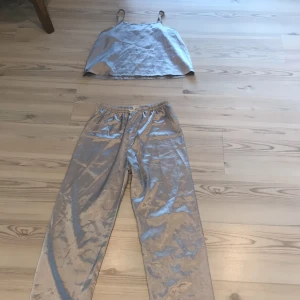 Silvrig Pyjamas med spetsdetaljer - Säljer en fin silvrig pyjamas. Inte använd så mycket. Båda delar i storlek 150. Spetsdetaljer längs ner på byxorna och även en liten rosett vid midjan på byxorna. 