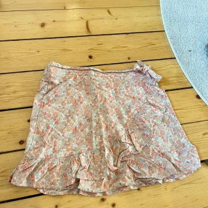 Blommig kjol med volang - Charmig blommig kjol i ljusa färger med volangdetaljer och knytning i midjan. Perfekt för en somrig look.