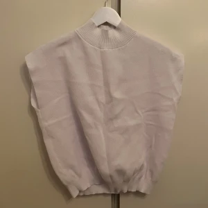 Vit väst - OANVÄND - Säljer en stilren vit väst med hög krage. Perfekt för lager-på-lager under kyligare dagar. Västen har en ribbad kant vid kragen och nederkanten för en snygg passform.