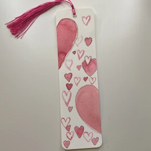 Handgjord bokmärke med hjärtan - Charmigt handgjort bokmärke med rosa och röda hjärtan i olika storlekar. Bokmärket har en rosa tofs upptill för enkel hantering. Perfekt alla hjärtans dag present till någon som älskar att läsa! 💖Det går självklart att byta färg på tofsen hör bara av er!