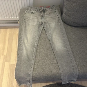 Grå jeans från Guess - Snygga grå jeans från Guess med klassisk femficksdesign och dragkedja. De har en stilren look med märkets logga på bakfickan. Perfekta för en avslappnad stil. Använd knappast. Ny pris ligger på 900-1100