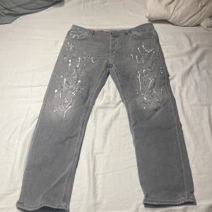 Grå jeans med färgstänk från Dondup - Snygga grå jeans från Dondup med unika vita färgstänk för en cool look. Byxorna har en rak passform och är en del av en limited edition-kollektion. Perfekta för dig som vill sticka ut med stil.