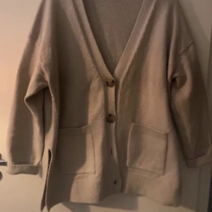 Stickad kofta - Mysig beige kofta med stora knappar framtill och två fickor. Den har en avslappnad passform och långa ärmar, perfekt för kyliga dagar. Jätte snygg men säljer då jag tycker att den sitter lite för oversized på mig