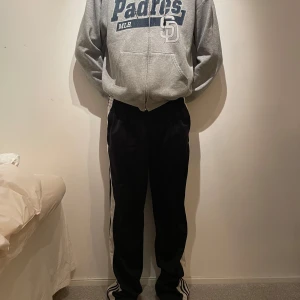 Svarta byxor från Adidas - Svarta träningsbyxor från Adidas med vita ränder längs sidorna och knappar. Passar både mig som brukar ha storlek 38 (damstorlek) och han på bilden. 