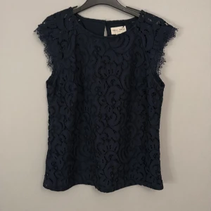 Svart spetsblus från Holly & Whyte Lindex - Elegant marinblå spetsblus från Holly & Whyte by Lindex. Blusen är ärmlös med vackra spetsdetaljer och en knapp i nacken. 
