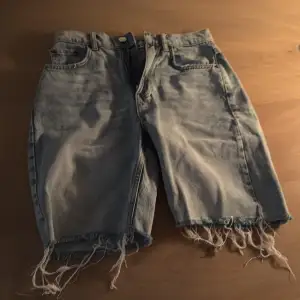 Säljer ett par ljusblå jeansshorts med fransiga kanter. En längre modell.  De har en klassisk femficksdesign och knappgylf. Perfekta för en avslappnad stil.
