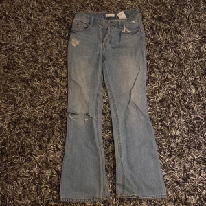 Ljusblå bootcut jeans - Snygga ljusblå bootcut jeans med slitna detaljer på låret och knäet. Perfekta för en avslappnad stil. Klassisk femficksdesign och knappgylf.