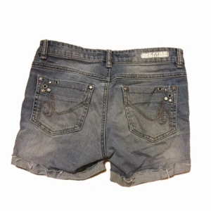 Jeansshorts från Lab Industries - Snygga jeansshorts från Lab Industries med coola dragkedjedetaljer framtill och dekorativa sömmar på bakfickorna. Shortsen har en klassisk blå jeansfärg och fransiga kanter. (färgen skiftar lite från bilderna) 