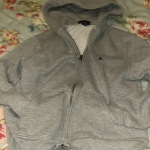 Grå hoodie från Polo Ralph Lauren - Säljer en klassisk grå hoodie från Polo Ralph Lauren. Den har en dragkedja framtill och en bekväm huva. Perfekt för en avslappnad stil. Passar bra till både jeans och joggers.