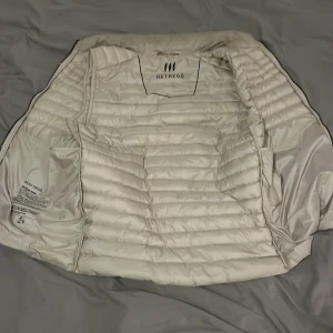 Vit quiltad dunväst från Hetrego - Säljer en snygg vit quiltad dunväst från Hetrego. Västen har en dragkedja framtill och två praktiska fickor med dragkedjor. Perfekt för lager-på-lager under höst och vår. Den är i bra skick och redo för nya äventyr!