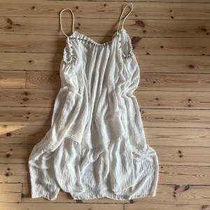 Vit sommarklänning med pärldetaljer - Säljer en superfin vit klänning! Den är ärmlös med tunna axelband och har snygga pärldetaljer i silver längs halsringningen och ärmhålen. Materialet är lätt och luftigt. Klänningen har en lös passform. Jag älskar den. Vill ej sälja egentligen