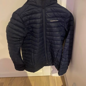 Svart dunjacka från Peak Performance - Säljer en marinblå dunjacka från Peak Performance. Den är quiltad och har en dragkedja framtill. Perfekt för kyliga dagar. Jackan är i bra skick men har en liten lagning på ena ärmen. Tveka inte att höra av er vid funderingar.