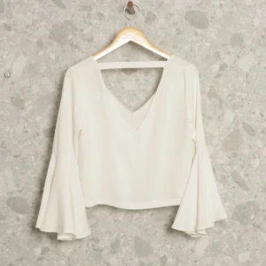 Vit blus med vida ärmar - Säljer en superfin vit blus med vida ärmar och v-ringning. Den är croppad och har en luftig passform, perfekt för både vardag och fest. Materialet känns mjukt och bekvämt.